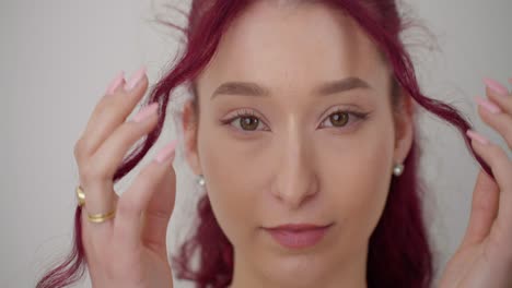 primer plano de una hermosa joven caucásica tocando el cabello rosa púrpura mirando a la cámara