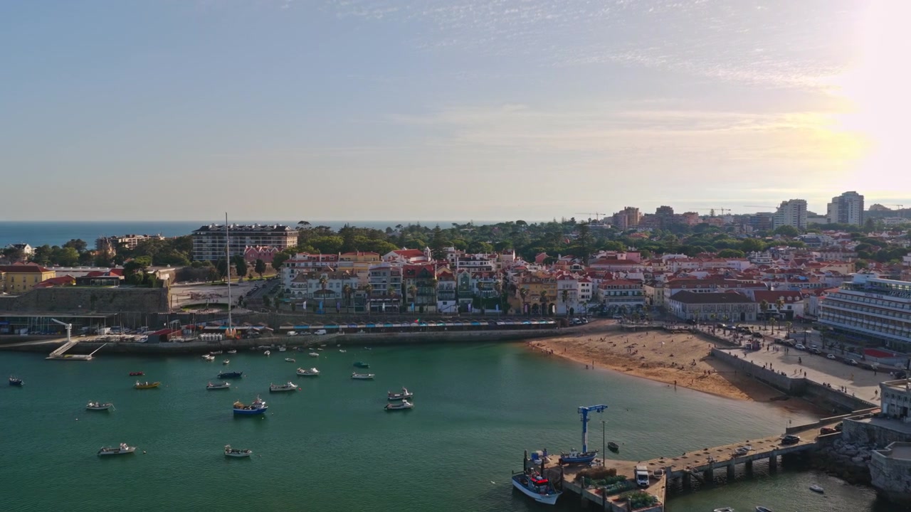 Vista de dron de Praia da Ribeira, el paseo marítimo de Cascais y barcos anclados en la Bahía de Cascais, Portugal, durante la cálida luz de la hora dorada.