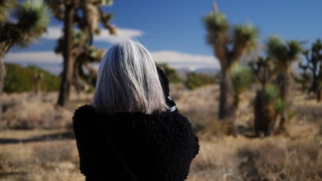 a woman taking photos with her old fashioned film camera and lens in a desert nature preserve park landscape