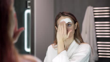 portrait of a woman in bathrobe putting white mask for moisturizing using fingers