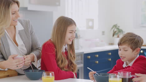 padres ayudando a los niños en uniforme escolar a prepararse mientras comen el desayuno en el mostrador de la cocina