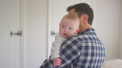 loving father cuddling smiling baby son resting over shoulder at home together - shot in low motion