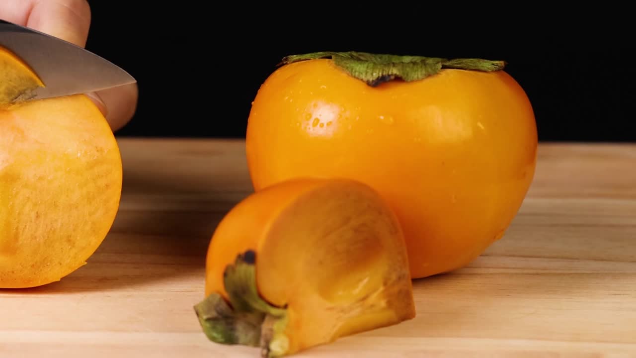 A detailed view of slicing a ripe persimmon on a wooden board with a sharp knife.