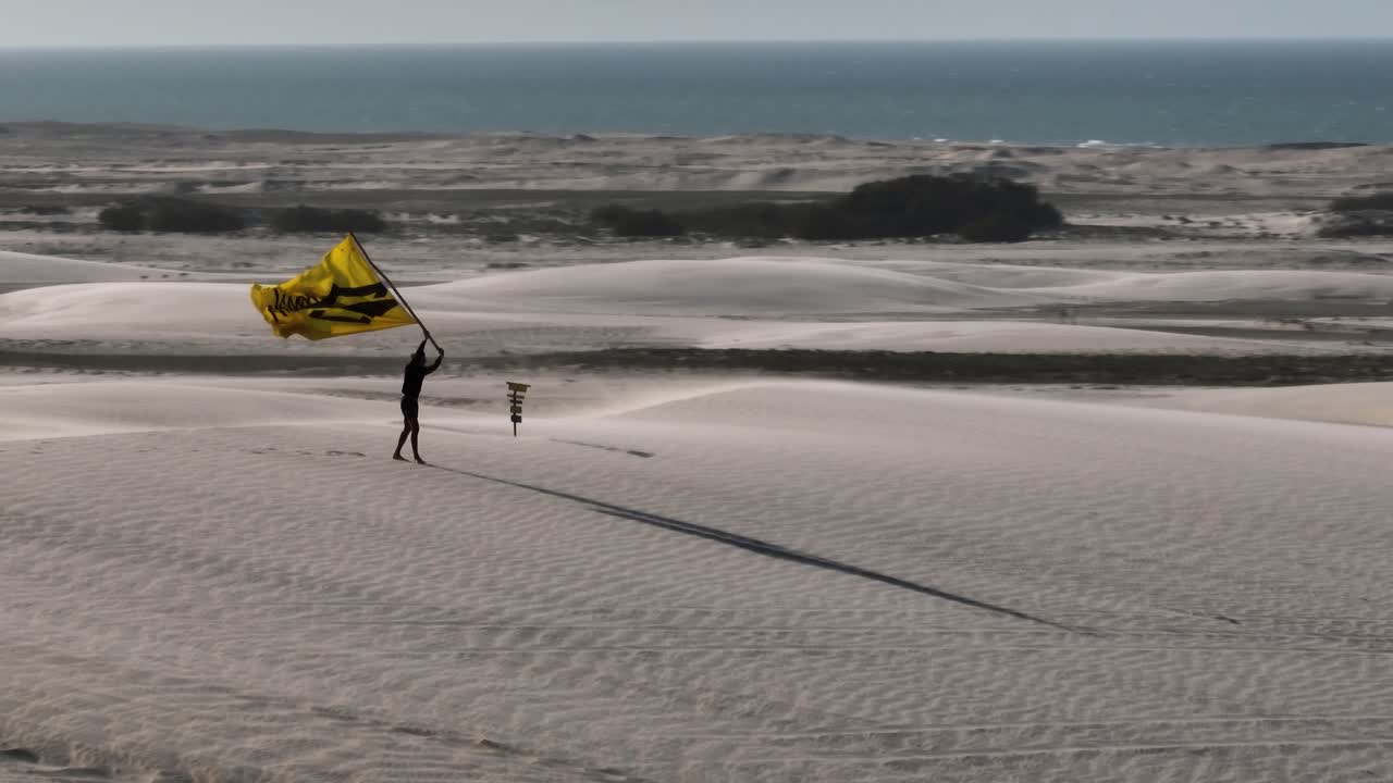 persona sosteniendo una bandera en un paisaje de dunas de arena blanca