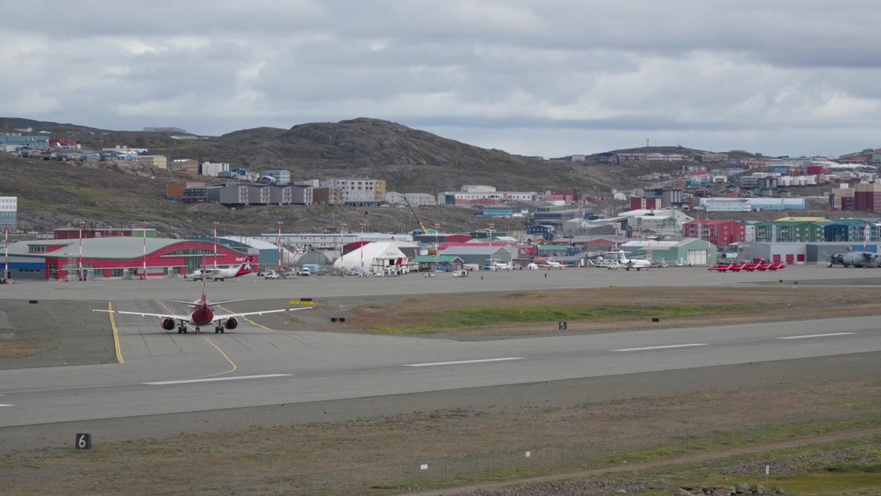 Bredt perspektiv som viser et passasjerfly fra Canadian North som takser på forplassen, med en rekke knallrøde RAF Red Arrows jagerfly parkert i bakgrunnen.