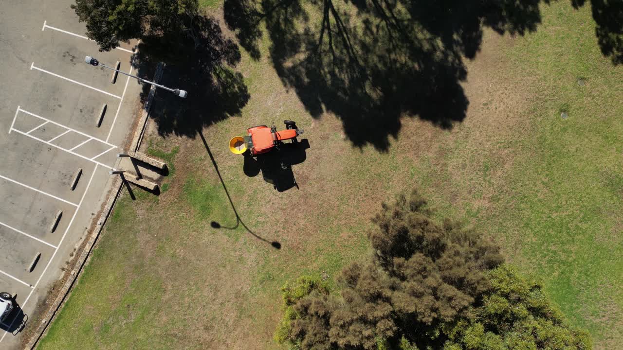 vista de arriba hacia abajo de un tractor naranja sembrando manchas desnudas en el césped de un parque