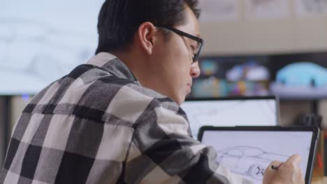 close up side view of asian male thinking about new car concept while working on a car design sketch on tablet in the studio with tv and computers display 3d electric car model