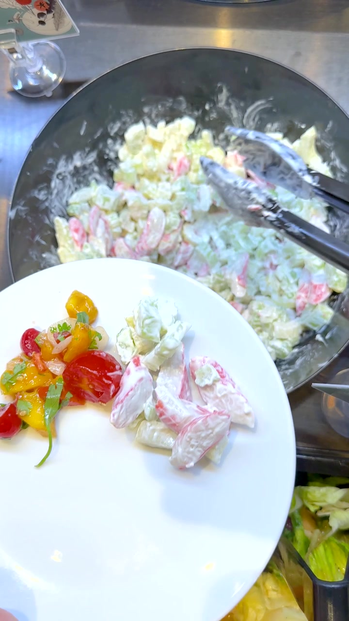 Ripresa dall'alto di pinze che servono insalata cremosa di surimi su un piatto a un buffet