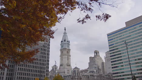 slow-motion shot of philadelphia’s historic city hall framed by swaying autumn tree branches, blending nature and architecture in a peaceful urban moment under a soft, cloudy sky.