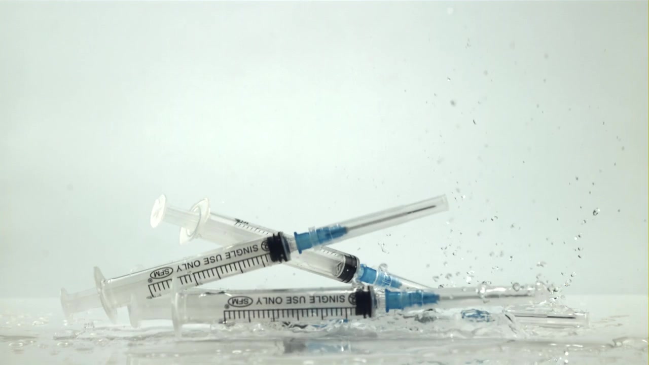 Siringhe mediche che cadono e schizzano su una superficie bagnata al rallentatore
