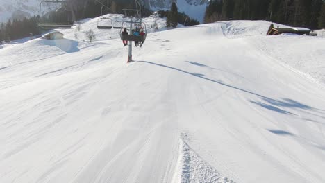 tomada desde un telesilla cuesta arriba con esquiadores en el fondo de picos montañosos nevados y esquiadores cuesta abajo