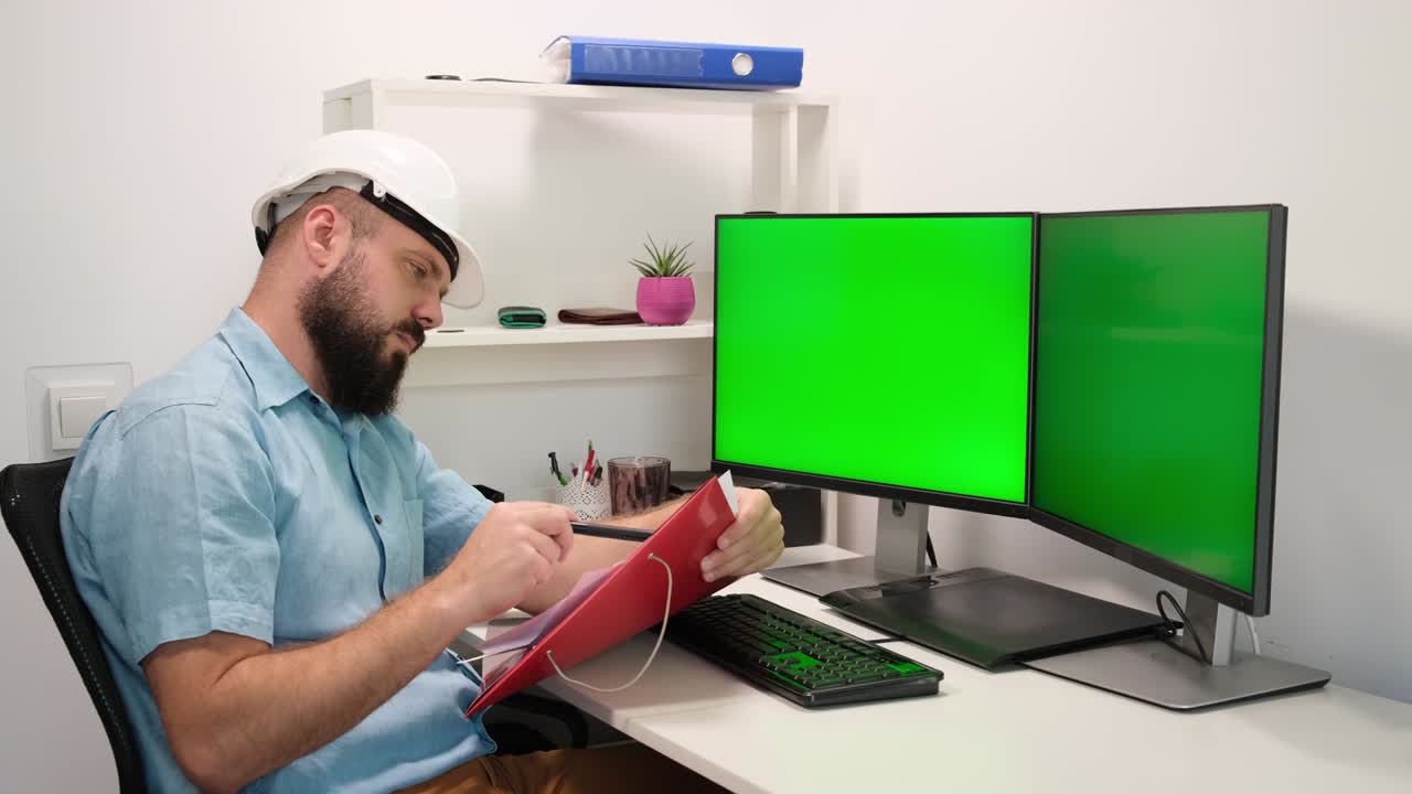 ingeniero con chaleco de seguridad y casco trabaja en una computadora, dos pantallas de monitor muestran clave de croma. pantalla verde muestra