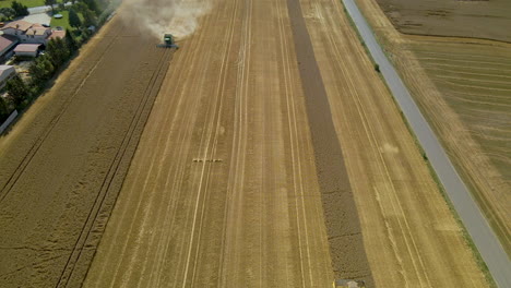 Tractors-Working-On-The-Golden-Field-During-Harvest-Season-In-Kielno,-Poland---tilt-down-pullback-drone-shot
