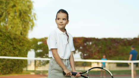 Retrato-De-Una-Chica-Guapa-Con-Un-Polo-Blanco-Parada-Al-Aire-Libre-En-La-Cancha-De-Tenis-Y-Sosteniendo-Una-Raqueta