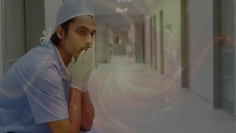 Animation-of-moving-spiral-over-sad-biracial-male-nurse-in-hospital