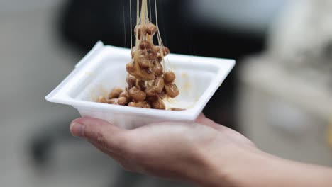 person eating sticky natto from a takeout container