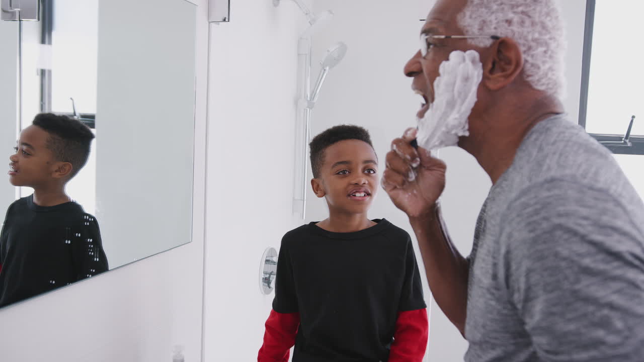 Grandfather Wearing Pajamas In Bathroom Shaving Whilst Grandson Watches