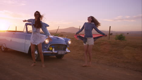 girl friends dancing at sunset on road trip with vintage car