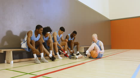 basketball team preparing for game, tying shoes and holding ball in gym
