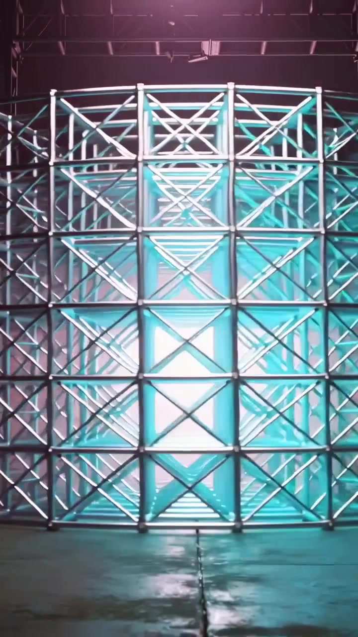 Video verticale: Luci che si spostano illuminando un cubo a traliccio su pavimento lucido, rivelando retroilluminazione e foschia.