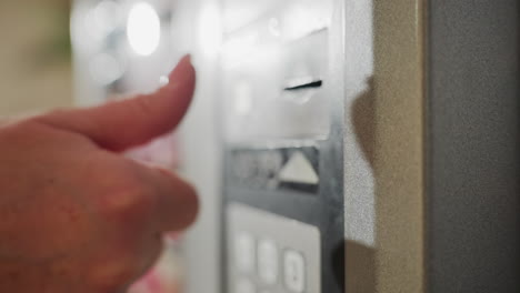 close-up of hand inserting key into digital safe lock panel, attempting to access secured storage or safe, with keypad and metal surface in view