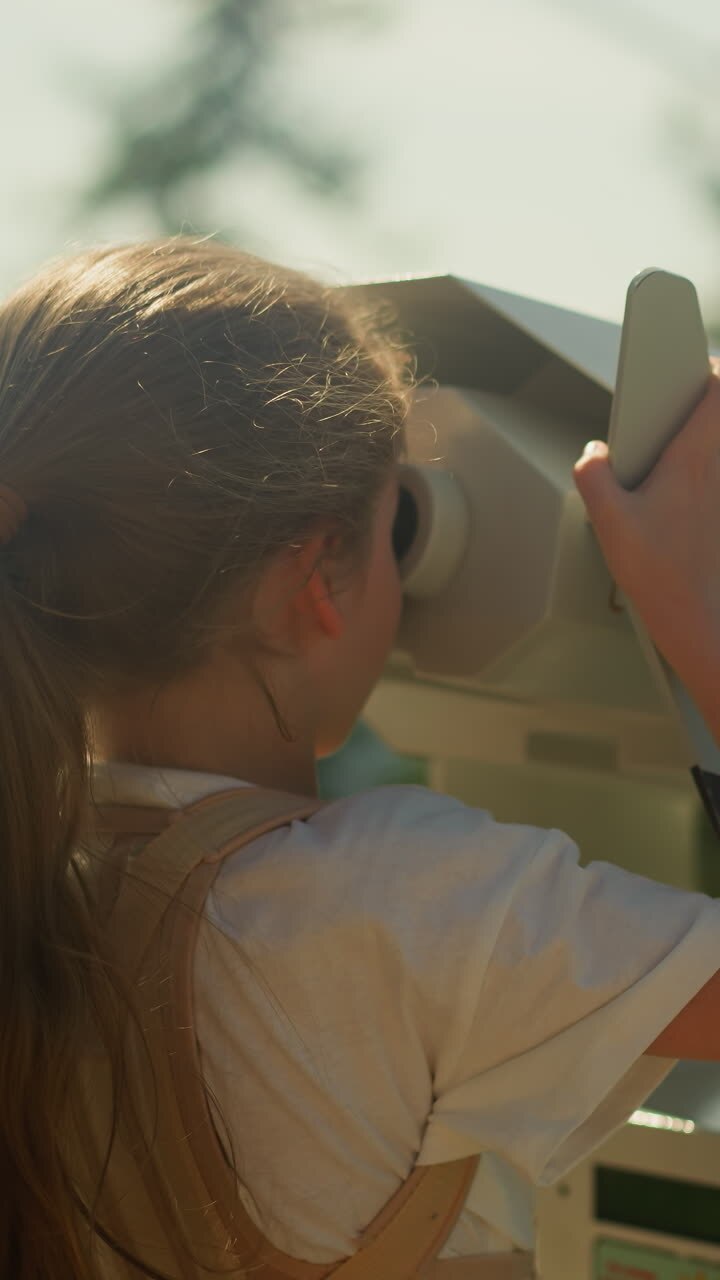 Curious girl explores stunning natural scenery of mountainous region through binoculars at well visited tourist spot on summer holiday. Childhood memory slow motion