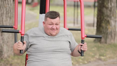 overweight young man exercising on sports equipment in the park overweight young man exercising on sports equipment in the park fat man works slowly outdoors active lifestyle as antiobesity