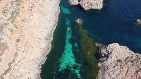 Drone-view-of-a-yellow-kayak-in-the-Mediterranean-sea,-turquoise-water-of-Blue-lagoon-Comino,-Malta-Island