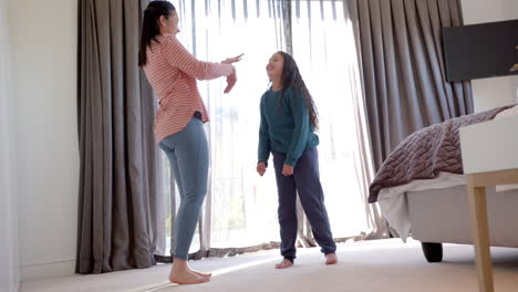 Happy-biracial-mother-and-daughter-dancing-in-sunny-bedroom