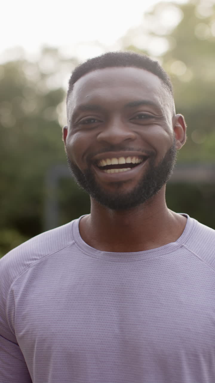 Vertical video portrait of happy african american man smiling in garden, in slow motion