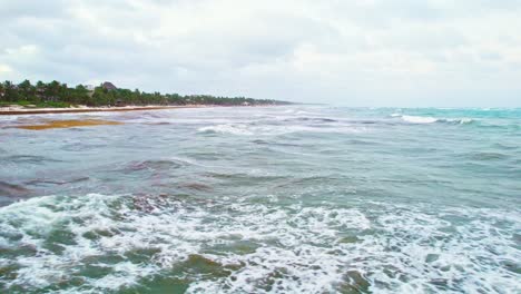 Gelber-Algen-Sargassum-Schwimmt-über-Türkisblauen-Strandwasserwellen-Mit-Bewölktem-Himmel-Im-Hintergrund