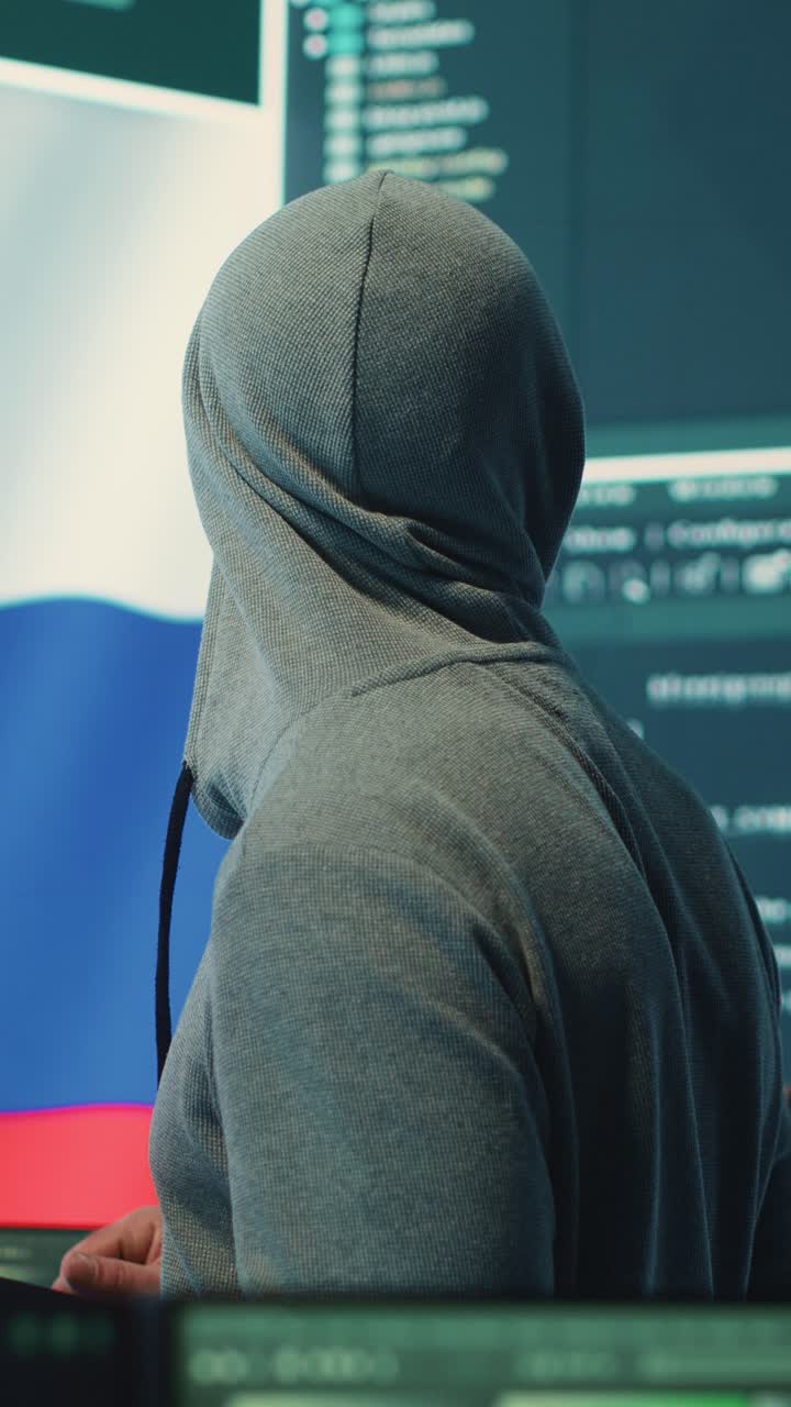 Uomo con felpa con cappuccio che lavora su schermi di computer con bandiera russa