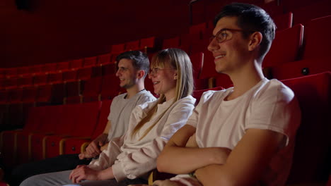 teenage girl and two boys smiling, watching a movie in a cinema, handheld shot