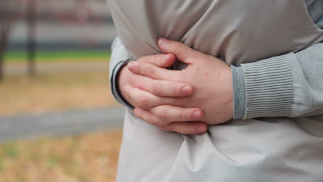 Close up of person holding individual closely around waist in gentle embrace, fingers spread on light jacket, showing warmth and affection, with blurred background featuring person riding scooter