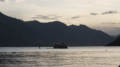 Sightseeing-tourist-boat-returns-to-Queenstown-harbor-at-sunset,-accompanied-by-seagulls