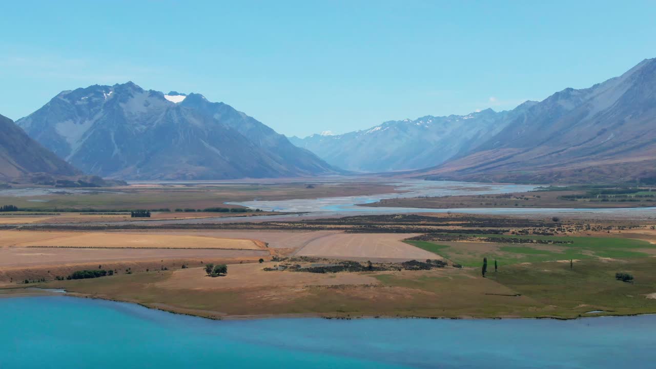 Panning footage of a golden landscape with farms nestled in a valley with distant mountains