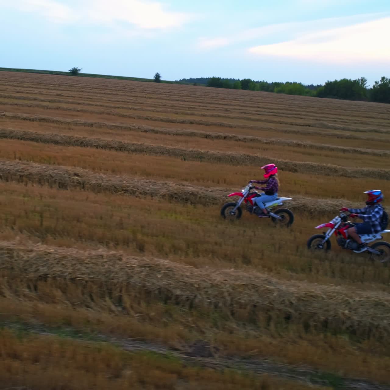 Happy young couple having fun riding motorbikes outside the city. Pair go by motorcycles wearing helmets. Mowed wheat field at backdrop