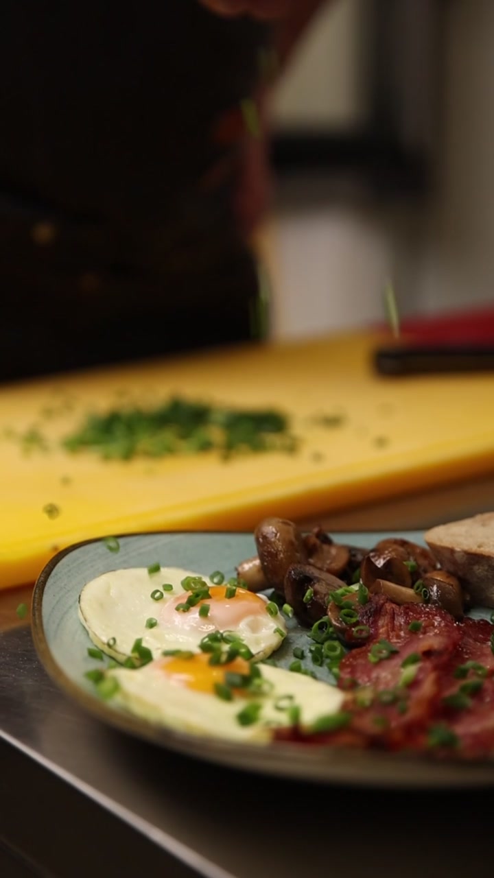 Chef che cosparge cipollina su un delizioso piatto per la colazione