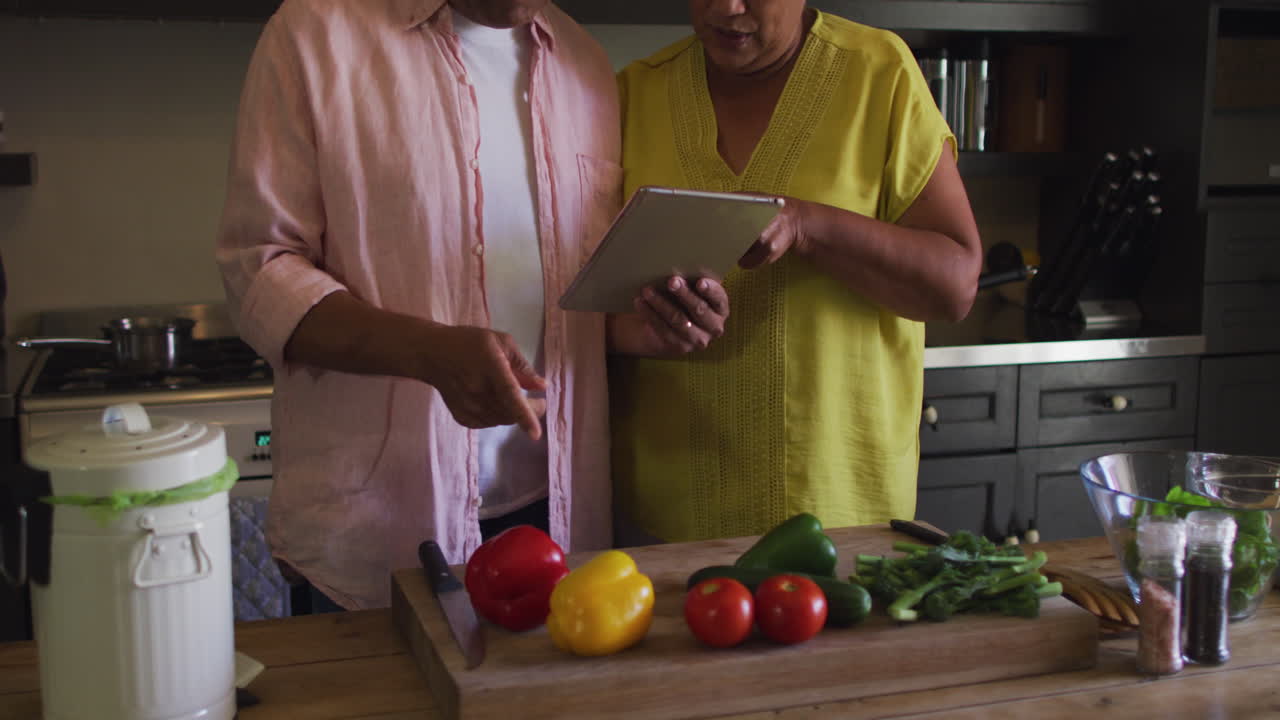 una pareja de dos razas que usa una tableta preparando comida en la cocina.