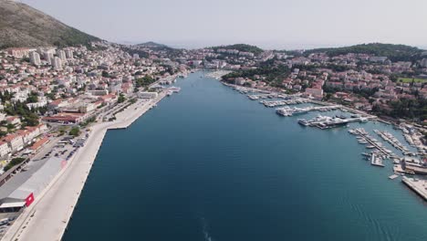 Dolly-Aéreo-Panorámico-Ingresa-Al-Puerto-De-Dubrovnik,-Croacia,-Mientras-La-Ciudad-Se-Extiende-Por-Las-Montañas