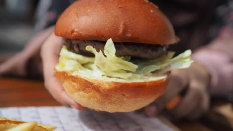 Hand-holding-beef-burger-on-table-close-up