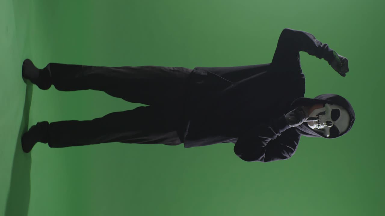 녹색 스크린 배경에 칼을 들고 침을 제스처하는 할로윈 마스크를 입은 후드 스웨트 셔츠를 입은 무서운 남자