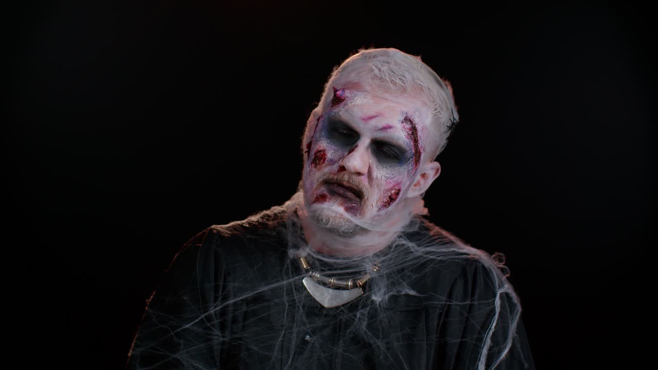 Sinister man with horrible scary Halloween zombie makeup in convulsions making faces trying to scare