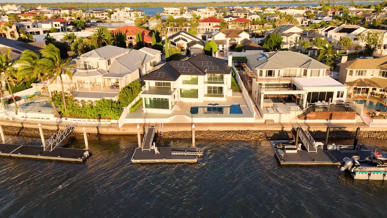 Drone footage captures luxurious waterfront estates along Gold Coast's serene river at sunset, highlighting architectural elegance and tranquil surroundings