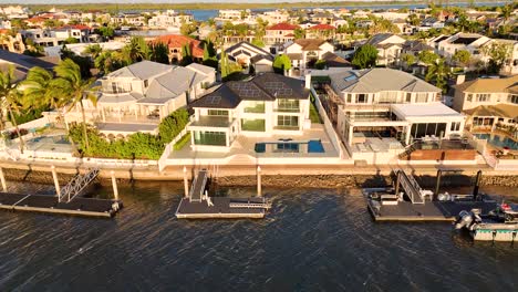 drone footage captures luxurious waterfront estates along gold coast's serene river at sunset, highlighting architectural elegance and tranquil surroundings