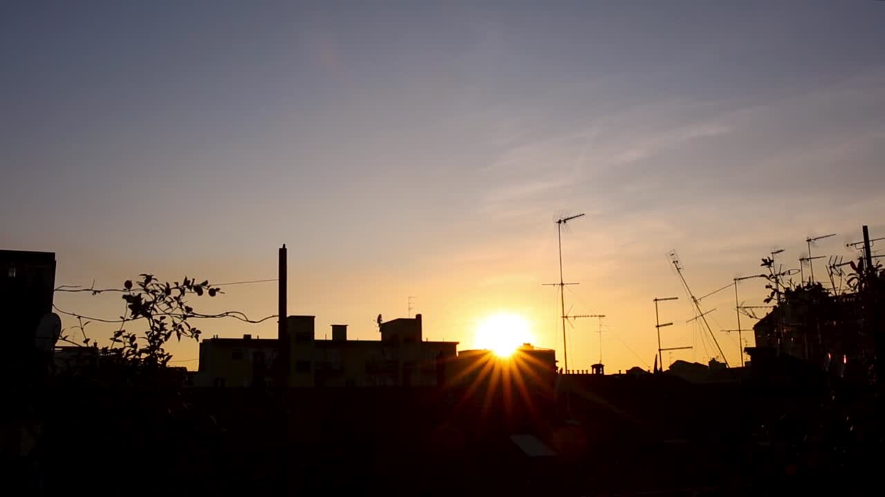 Vista de tejados de edificios en silueta con un cielo nublado naranja y azul al fondo.