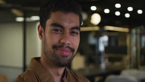 Portrait-of-a-mixed-race-businessman-looking-at-camera-and-smiling-in-modern-office
