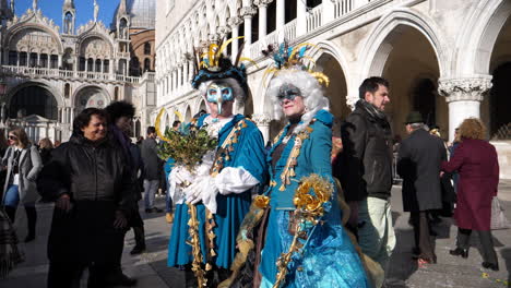 masked couple with blue costumes, posing in st mark's square. venice carnival