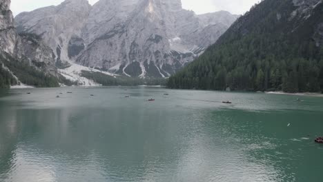 Drone-video-with-a-diagonal-plane,-over-the-lake-of-braies-with-boats-with-people-rowing-and-mountains-on-the-horizon