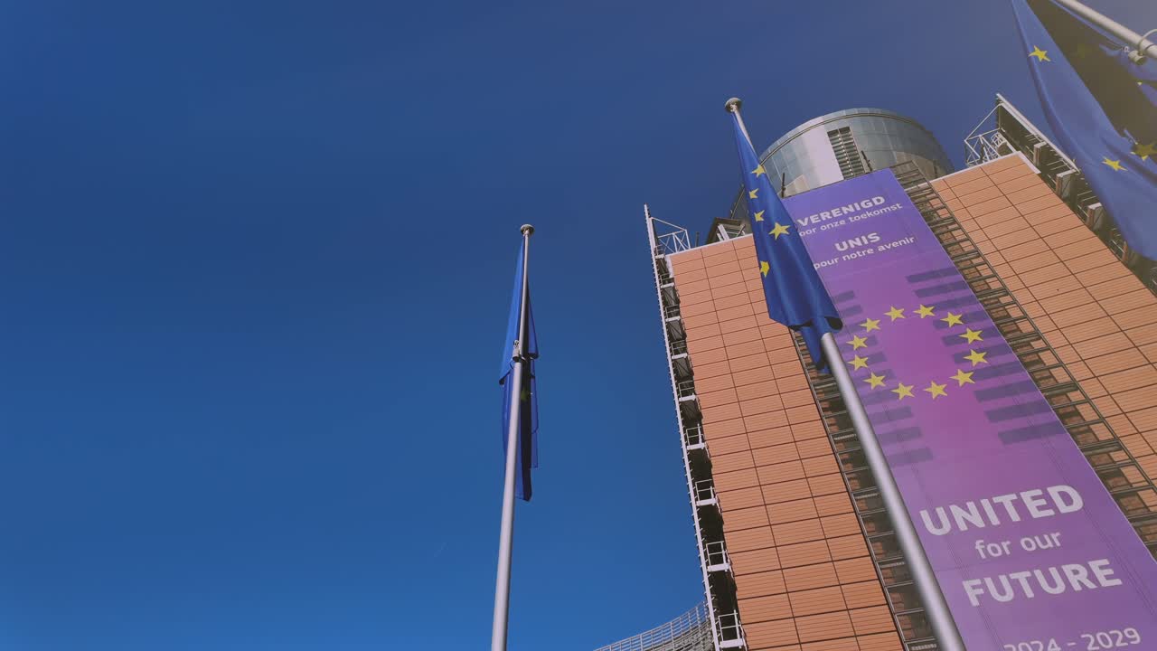 Low-angle view of EU Commission building with flags and banner